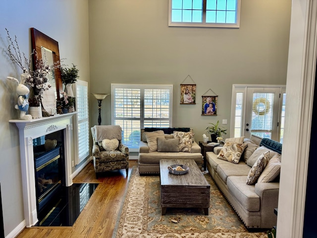 living area with a towering ceiling, a fireplace with flush hearth, and wood finished floors