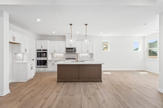 kitchen with pendant lighting, stainless steel appliances, light countertops, a kitchen island with sink, and white cabinetry