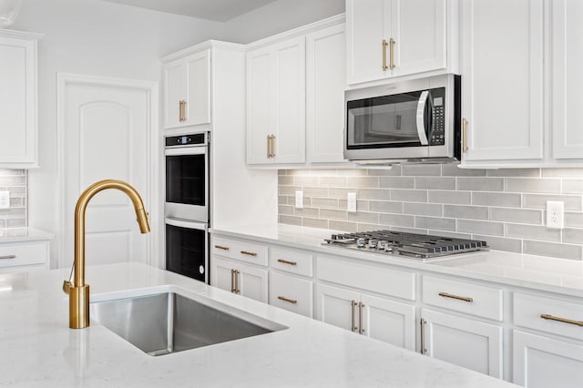 kitchen featuring stainless steel appliances, a sink, white cabinetry, light stone countertops, and tasteful backsplash