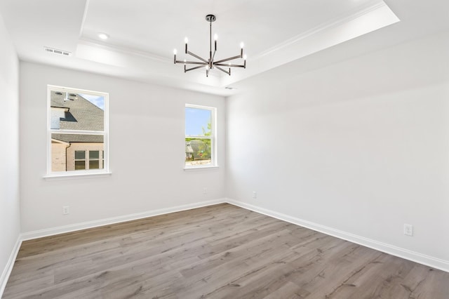 unfurnished room with a tray ceiling, light wood-type flooring, visible vents, and baseboards