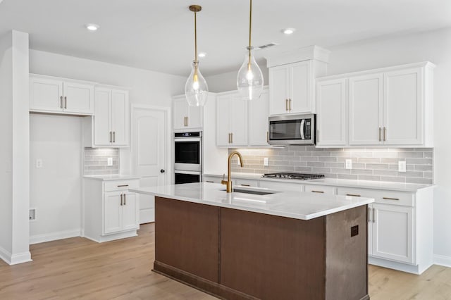 kitchen with stainless steel appliances, light countertops, hanging light fixtures, a kitchen island with sink, and white cabinets