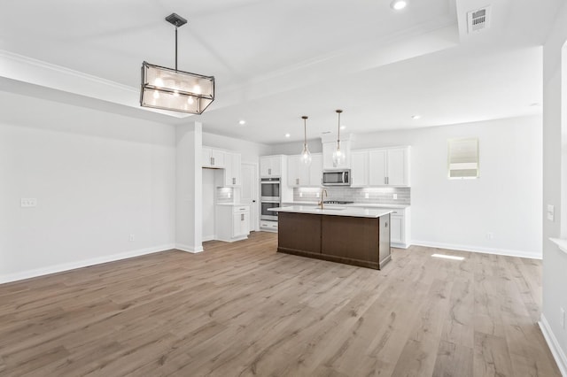 kitchen with a center island with sink, appliances with stainless steel finishes, decorative light fixtures, light countertops, and white cabinetry