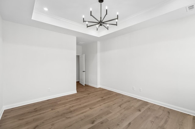 spare room with visible vents, a raised ceiling, baseboards, ornamental molding, and wood finished floors