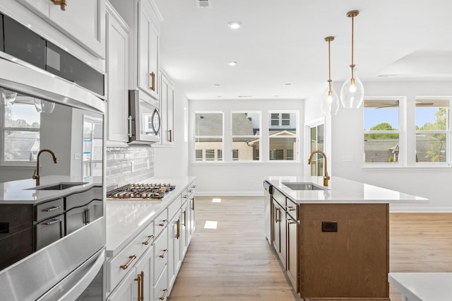 kitchen with light countertops, appliances with stainless steel finishes, a center island with sink, and white cabinets