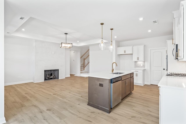 kitchen featuring a kitchen island with sink, white cabinets, light countertops, appliances with stainless steel finishes, and decorative light fixtures