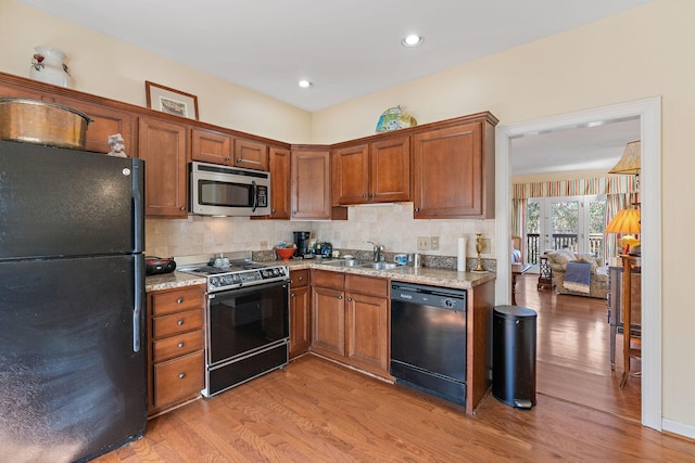 kitchen featuring light stone counters, a sink, black appliances, light wood finished floors, and tasteful backsplash