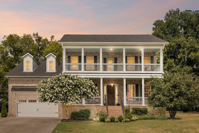 view of front of house featuring driveway, a balcony, a porch, a front lawn, and brick siding