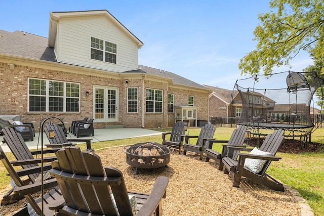 rear view of house featuring a shingled roof, a fire pit, a trampoline, a patio area, and brick siding