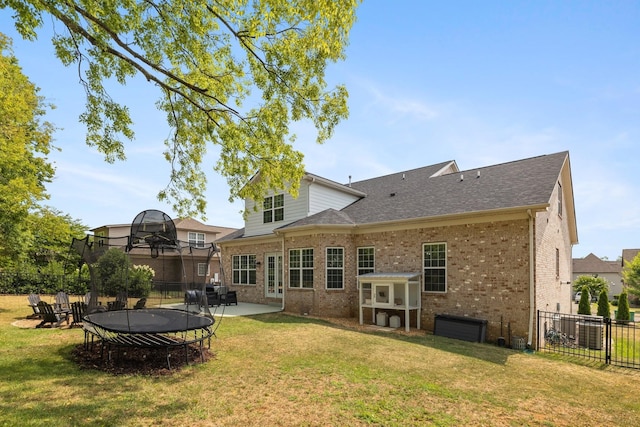 rear view of house featuring brick siding, a shingled roof, fence, a lawn, and a trampoline