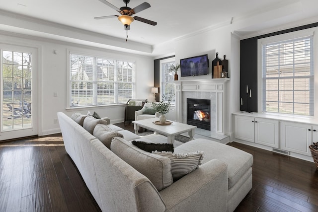 living area featuring dark wood finished floors, visible vents, ornamental molding, a glass covered fireplace, and baseboards