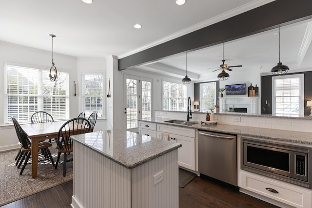 kitchen with a sink, white cabinetry, open floor plan, appliances with stainless steel finishes, and decorative light fixtures