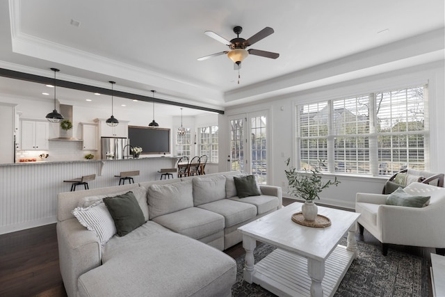 living room with dark wood-type flooring, a raised ceiling, crown molding, and a ceiling fan