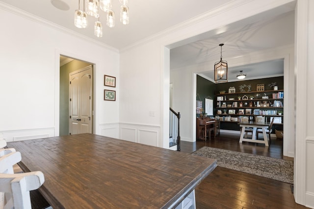 dining area with a wainscoted wall, ornamental molding, dark wood-style flooring, a chandelier, and a decorative wall