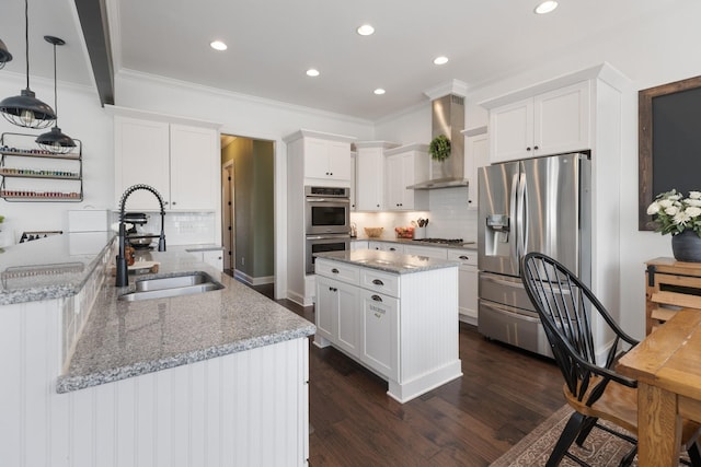 kitchen with stainless steel appliances, a sink, white cabinets, wall chimney range hood, and decorative light fixtures