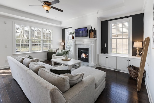 living area with dark wood-style flooring, plenty of natural light, a glass covered fireplace, and crown molding