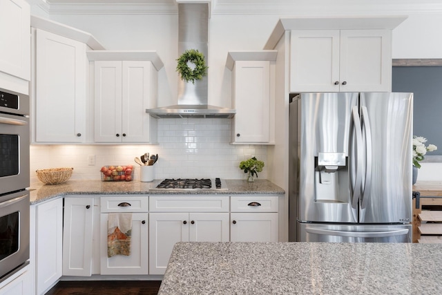 kitchen with light stone counters, stainless steel appliances, wall chimney range hood, white cabinetry, and backsplash