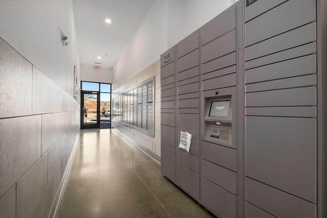 hallway featuring finished concrete flooring, a package area, mail area, and recessed lighting