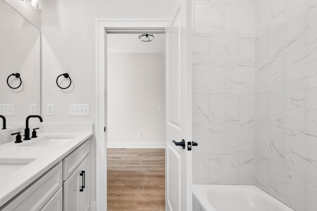 full bathroom featuring double vanity, baseboards, wood finished floors, washtub / shower combination, and a sink