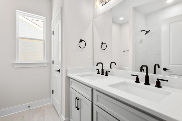 bathroom with double vanity, baseboards, walk in shower, and a sink