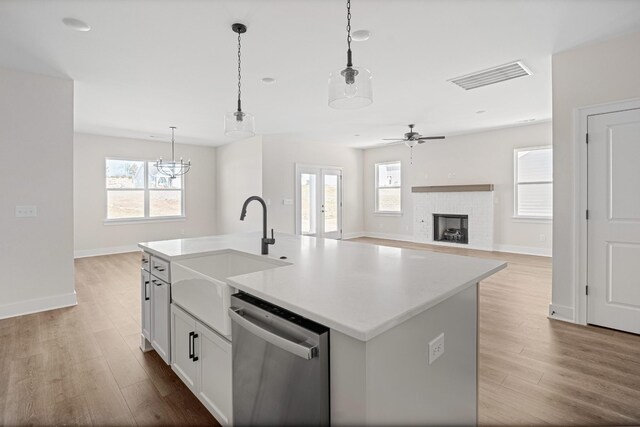 kitchen with wood finished floors, a sink, visible vents, stainless steel dishwasher, and decorative light fixtures