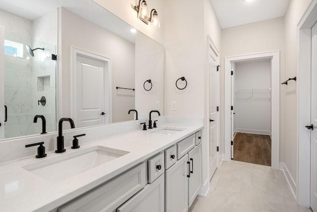 bathroom with a spacious closet, double vanity, a sink, and a marble finish shower