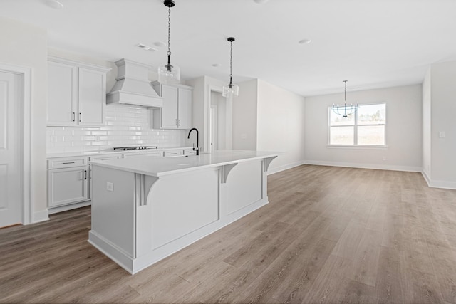 kitchen with light wood-type flooring, a center island with sink, custom exhaust hood, and light countertops