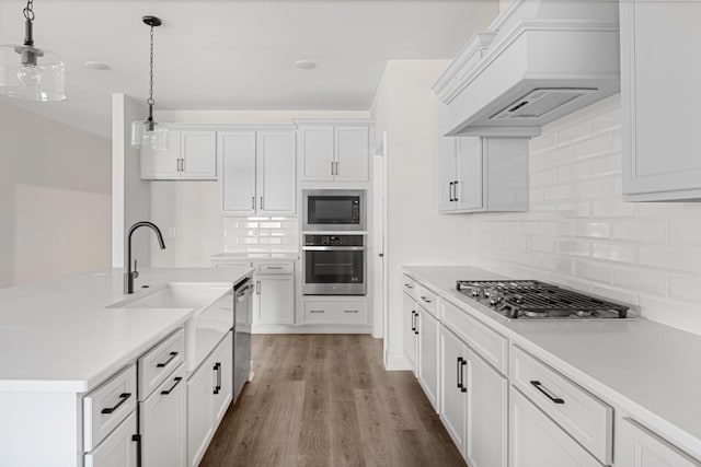 kitchen featuring light wood-style flooring, premium range hood, hanging light fixtures, appliances with stainless steel finishes, and light countertops