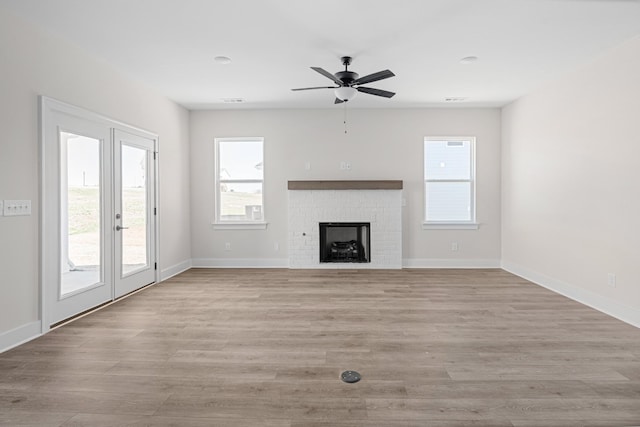 unfurnished living room with baseboards, light wood-type flooring, and a brick fireplace