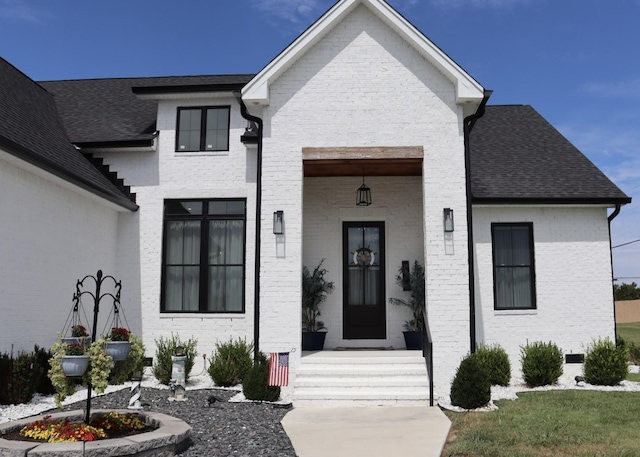 view of front facade with roof with shingles and brick siding