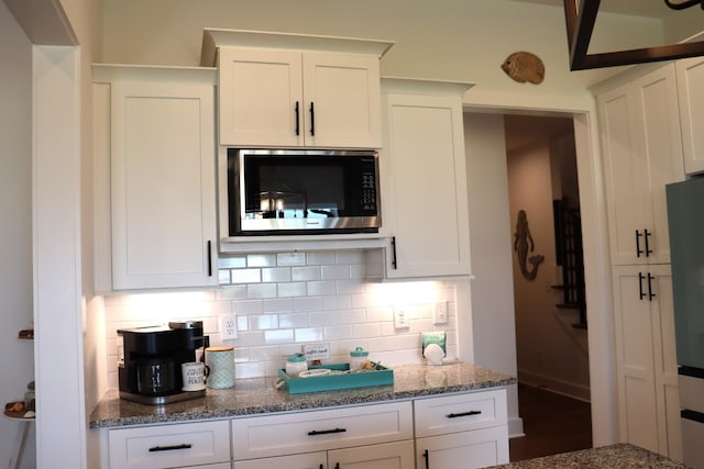 kitchen with stainless steel microwave, stone countertops, backsplash, and white cabinets