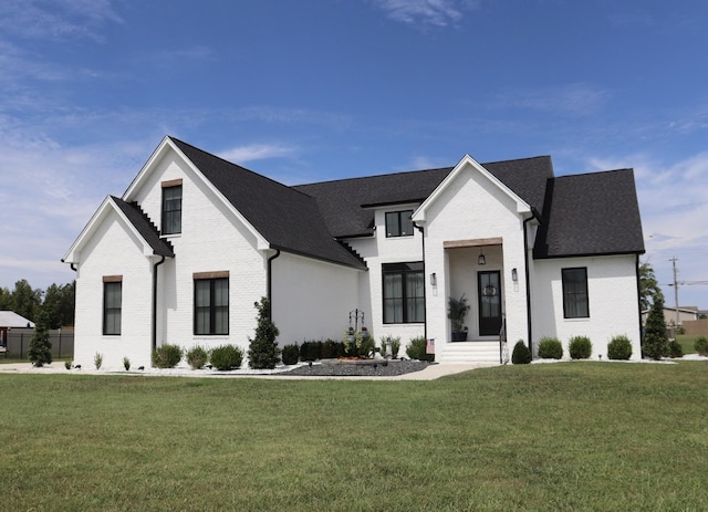 view of front of property featuring a shingled roof, brick siding, and a front lawn