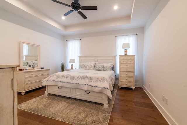 bedroom with a raised ceiling, dark wood finished floors, and baseboards