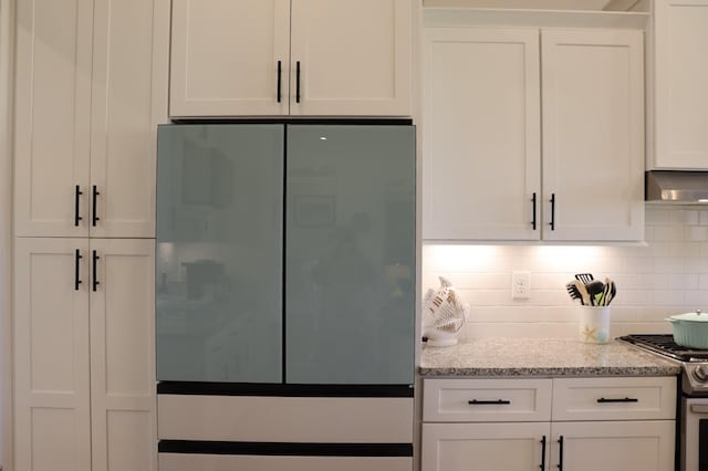 kitchen featuring white cabinets, gas range, light stone counters, refrigerator, and backsplash