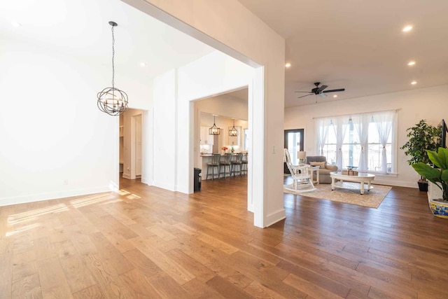 living room with ceiling fan with notable chandelier, baseboards, wood finished floors, and recessed lighting