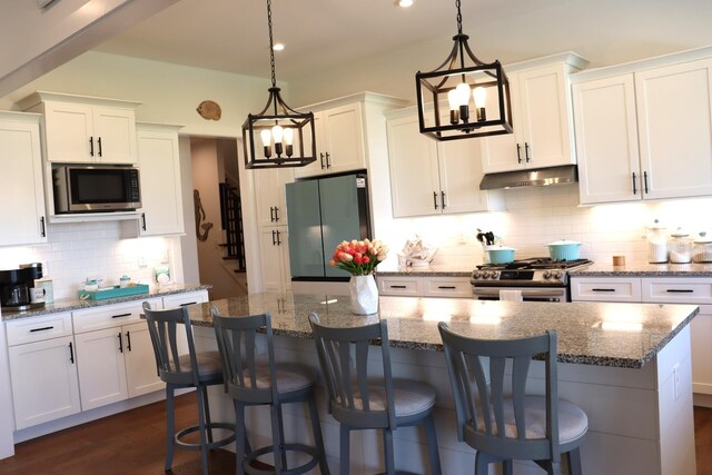 kitchen featuring a center island, gas stove, freestanding refrigerator, white cabinets, and under cabinet range hood