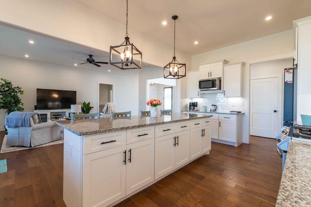 kitchen with white cabinets, stainless steel microwave, a kitchen island, and hanging light fixtures