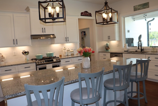 kitchen featuring a breakfast bar, gas stove, white cabinetry, a sink, and under cabinet range hood