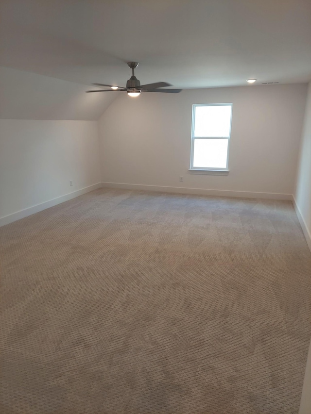 spare room featuring light carpet, ceiling fan, vaulted ceiling, and baseboards