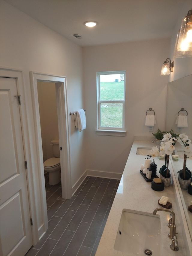 full bathroom with toilet, a sink, visible vents, baseboards, and double vanity