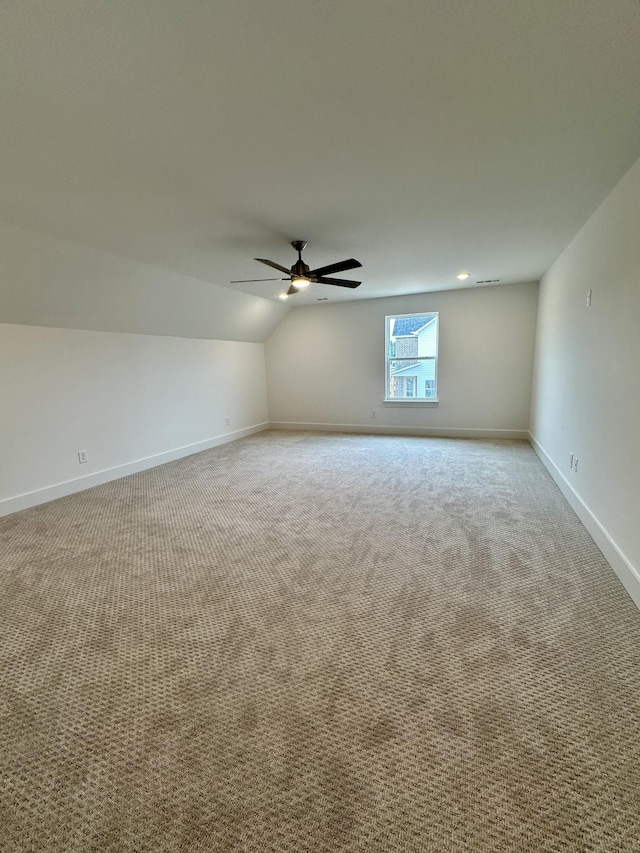 empty room with lofted ceiling, ceiling fan, baseboards, and light colored carpet