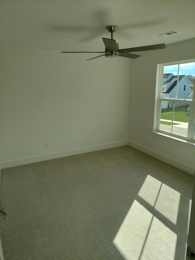 carpeted spare room featuring visible vents, a ceiling fan, and baseboards