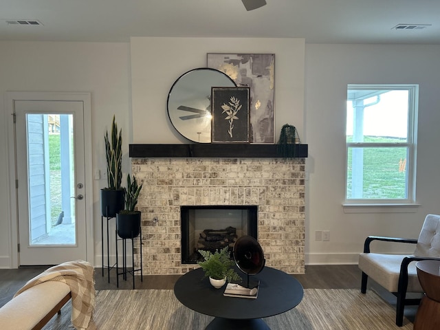 living room with dark wood-style floors, a brick fireplace, visible vents, and baseboards