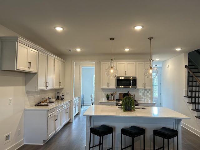 kitchen with a sink, white cabinetry, light countertops, appliances with stainless steel finishes, and pendant lighting