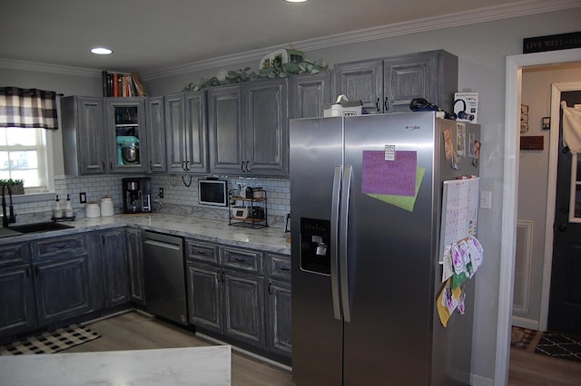 kitchen with light wood finished floors, light stone counters, ornamental molding, stainless steel appliances, and a sink