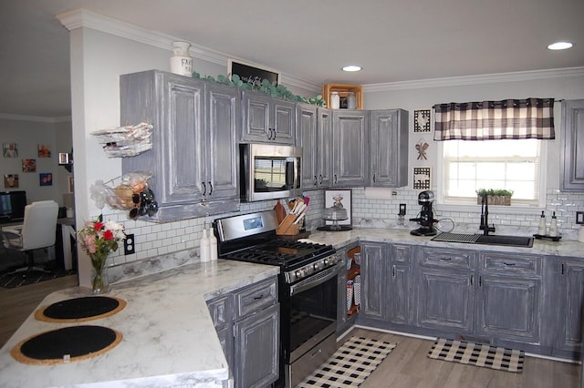 kitchen featuring light stone counters, stainless steel appliances, crown molding, light wood-type flooring, and a sink