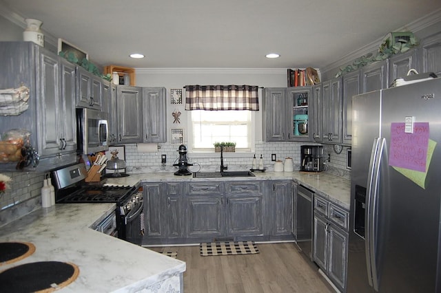 kitchen with stainless steel appliances, a sink, light wood-style floors, ornamental molding, and light stone countertops