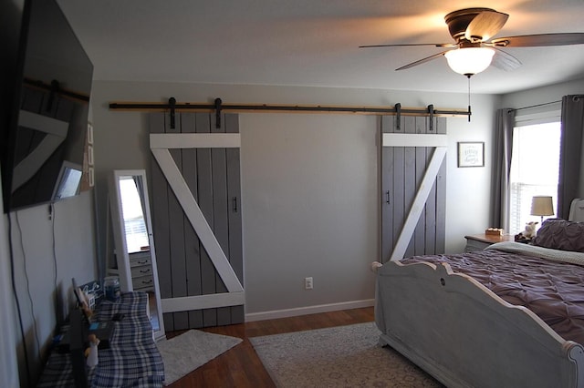 bedroom featuring a barn door, baseboards, and dark wood finished floors