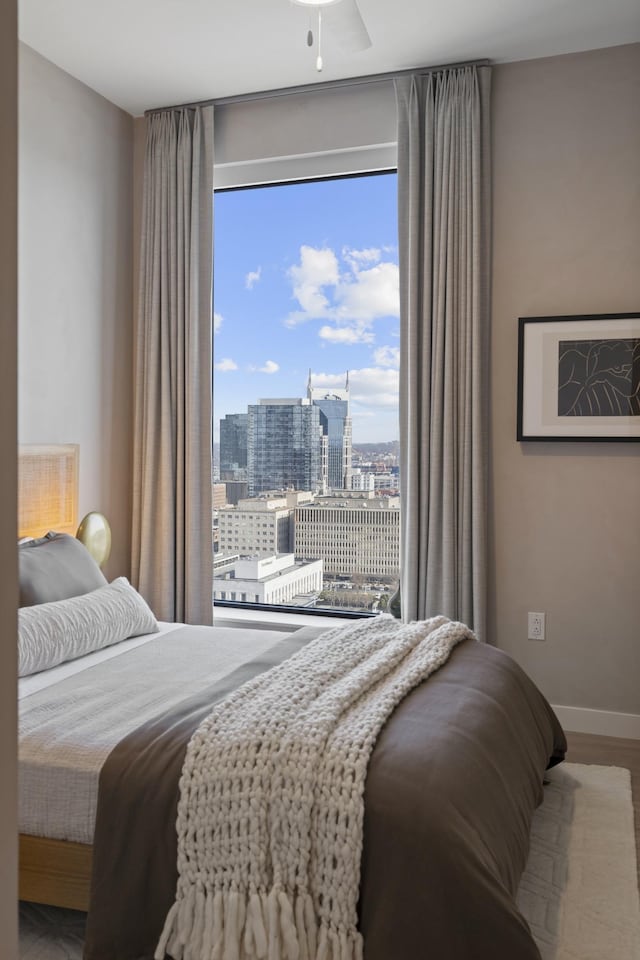 bedroom featuring wood finished floors, a view of city, baseboards, and a ceiling fan