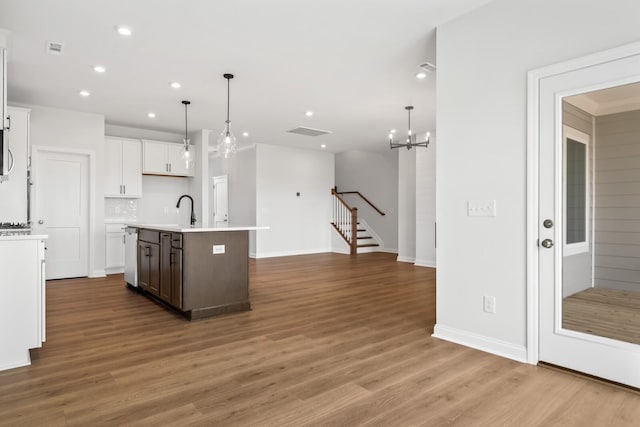 kitchen featuring wood finished floors, decorative light fixtures, a kitchen island with sink, light countertops, and white cabinetry