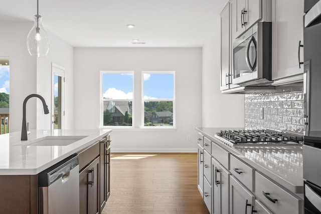 kitchen featuring wood finished floors, a sink, stainless steel appliances, pendant lighting, and backsplash